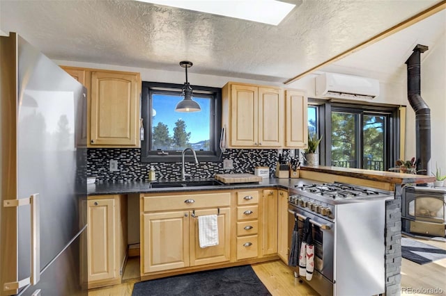 kitchen with stainless steel appliances, light brown cabinets, an AC wall unit, a sink, and a textured ceiling
