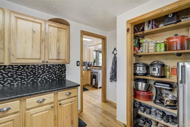 kitchen with light wood-style floors, decorative backsplash, light brown cabinetry, dark countertops, and high end stainless steel range