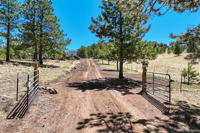 view of dirt / gravel driveway featuring a view of countryside, a gated entry, and a gate