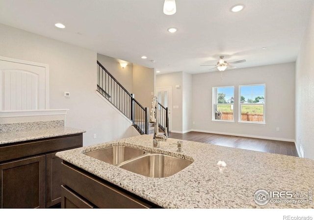 kitchen with sink, ceiling fan, dark brown cabinets, light hardwood / wood-style floors, and light stone counters