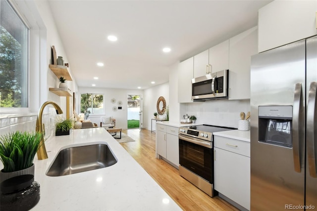 kitchen with white cabinetry, sink, light hardwood / wood-style flooring, decorative backsplash, and appliances with stainless steel finishes