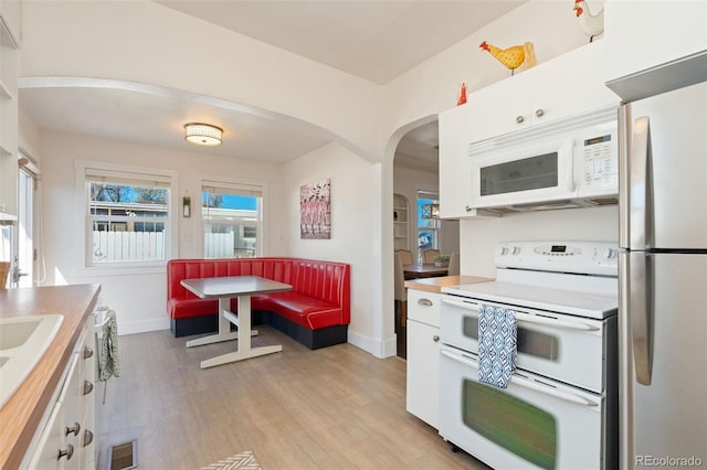 224 4th Ave, Severance, CO 80550 - kitchen with white appliances, arched walkways, white cabinetry, and light wood-style flooring