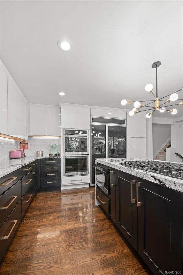 2062 Hyacinth Rd, Highlands Ranch, CO 80129 - kitchen featuring stainless steel appliances, light stone counters, white cabinets, a chandelier, and decorative light fixtures