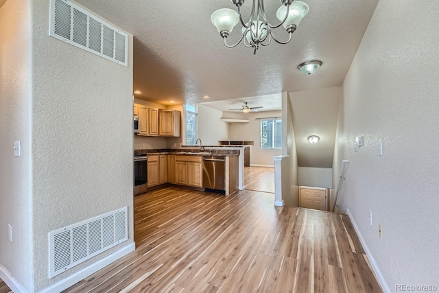 kitchen featuring light wood-type flooring, ceiling fan with notable chandelier, appliances with stainless steel finishes, decorative light fixtures, and kitchen peninsula