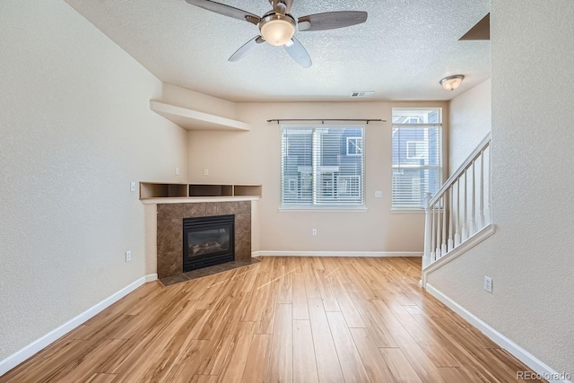 unfurnished living room with ceiling fan, light hardwood / wood-style flooring, a tiled fireplace, and a textured ceiling