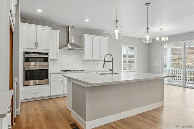 kitchen featuring light wood-type flooring, a sink, wall chimney range hood, and double oven