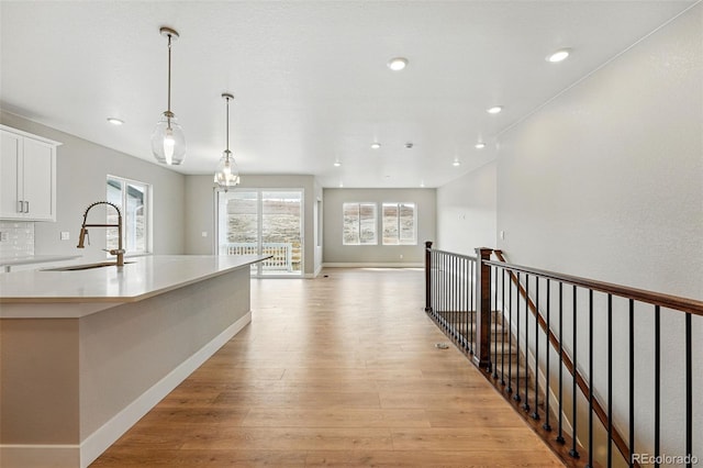 kitchen with hanging light fixtures, a sink, light countertops, white cabinetry, and light wood finished floors
