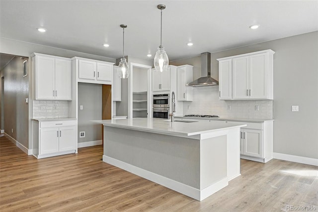 kitchen with white cabinets, tasteful backsplash, a center island with sink, and wall chimney exhaust hood