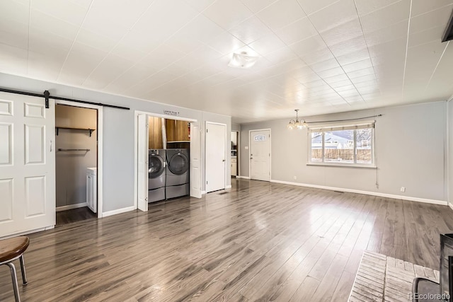 unfurnished living room featuring dark hardwood / wood-style floors, a barn door, separate washer and dryer, and an inviting chandelier