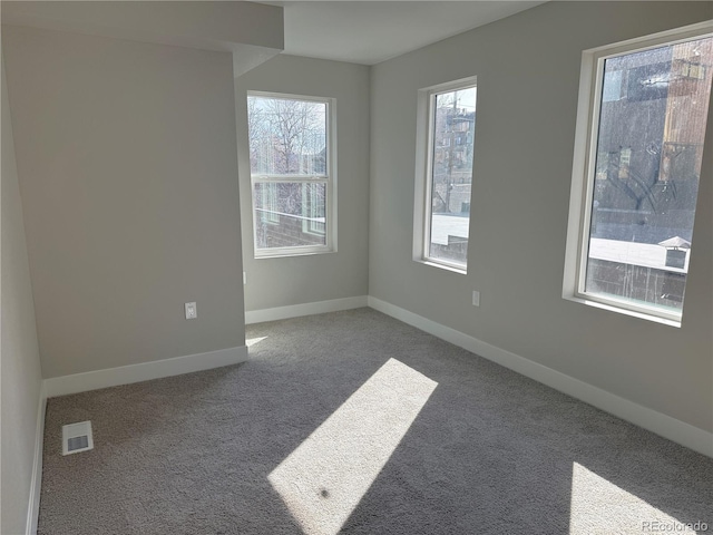 spare room featuring carpet floors, visible vents, and baseboards