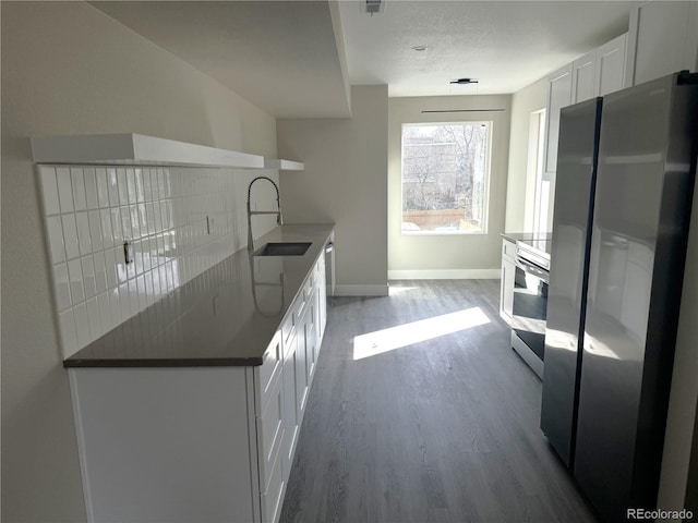 kitchen with freestanding refrigerator, baseboards, a sink, wood finished floors, and white cabinets