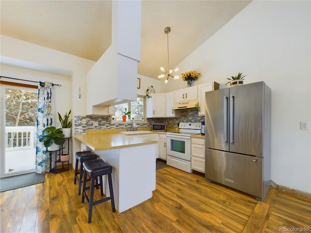 kitchen featuring a breakfast bar area, hanging light fixtures, high quality fridge, white range with electric stovetop, and white cabinets