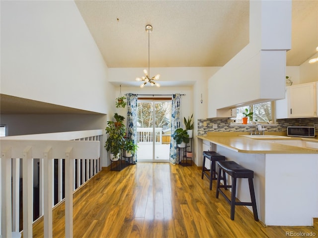 kitchen with dark wood-type flooring, a kitchen breakfast bar, decorative backsplash, white cabinets, and decorative light fixtures