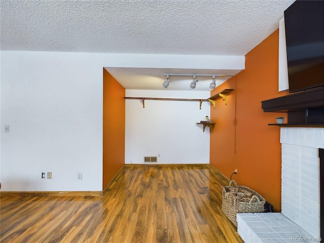 laundry room with dark hardwood / wood-style flooring, a brick fireplace, a textured ceiling, and rail lighting