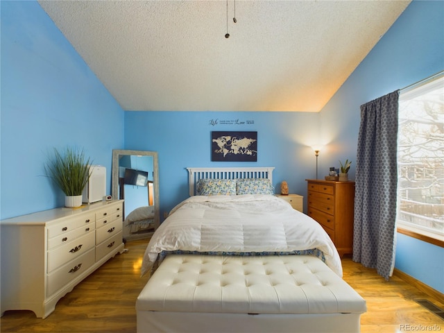 bedroom with lofted ceiling, a textured ceiling, and light hardwood / wood-style floors