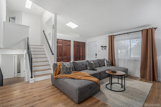 living room with stairway, a textured ceiling, lofted ceiling, and wood finished floors