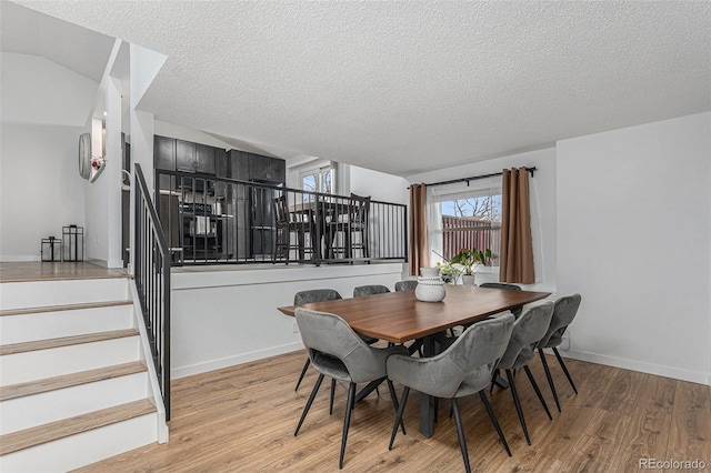 dining space featuring light wood-style flooring, a textured ceiling, stairs, and baseboards