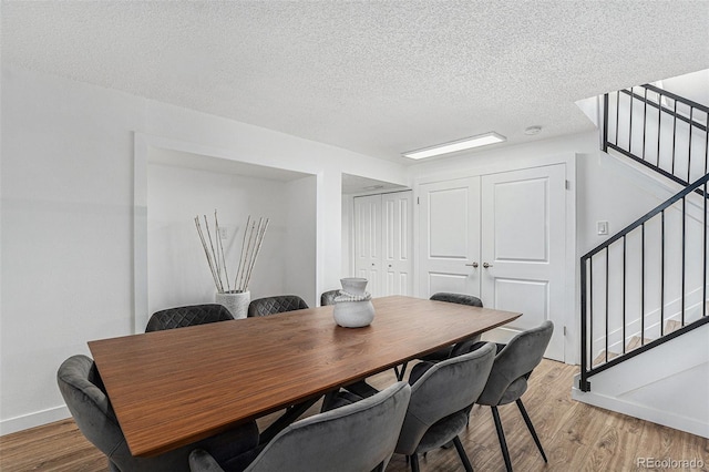 dining area featuring light wood-type flooring, baseboards, a textured ceiling, and stairs