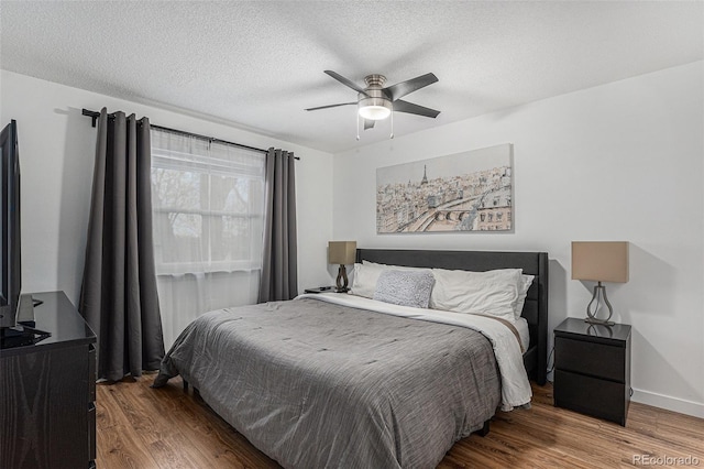 bedroom with ceiling fan, wood finished floors, baseboards, and a textured ceiling