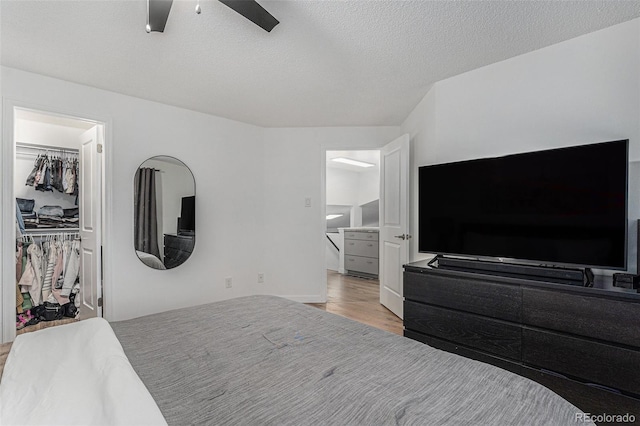 bedroom featuring wood finished floors, ceiling fan, a spacious closet, a closet, and a textured ceiling