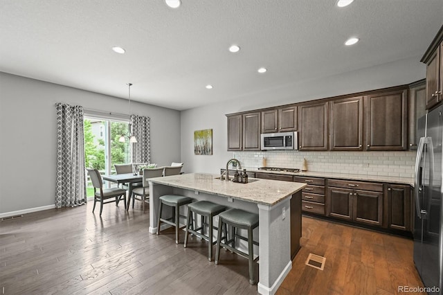 16256 Ute Peak Way, Broomfield, CO 80023 - kitchen with stainless steel appliances, tasteful backsplash, dark brown cabinets, a center island with sink, and recessed lighting