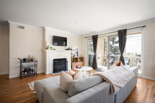 living area with a premium fireplace, visible vents, ornamental molding, and wood finished floors