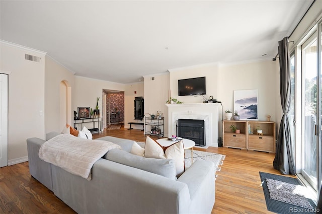 living area featuring visible vents, arched walkways, light wood-style flooring, and a high end fireplace