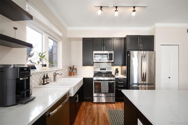 kitchen with a sink, light wood-type flooring, ornamental molding, stainless steel appliances, and dark cabinets