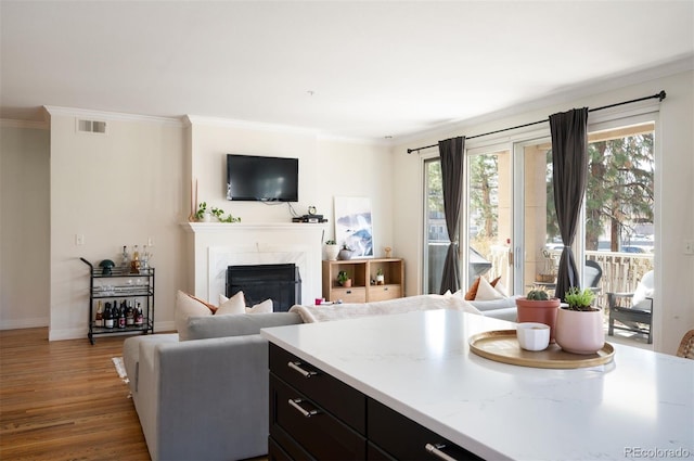 living room with wood finished floors, baseboards, visible vents, a high end fireplace, and ornamental molding