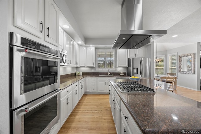 404 Yarrow Pl, Castle Pines, CO 80108 - kitchen featuring stainless steel appliances, island range hood, a sink, light wood finished floors, and white cabinetry