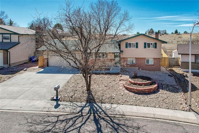 tri-level home featuring brick siding, fence, a chimney, a garage, and driveway