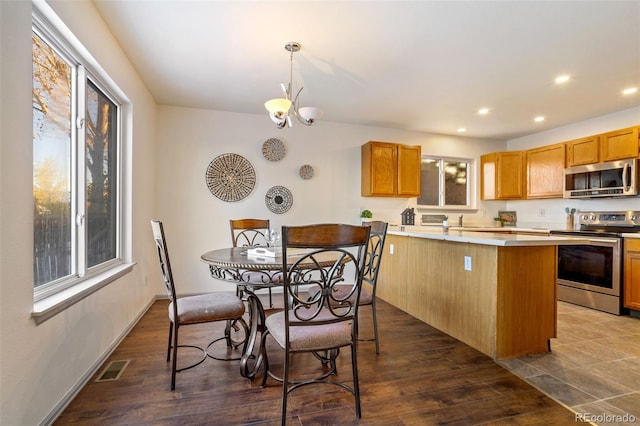 kitchen with hanging light fixtures, appliances with stainless steel finishes, a center island, dark wood-type flooring, and an inviting chandelier