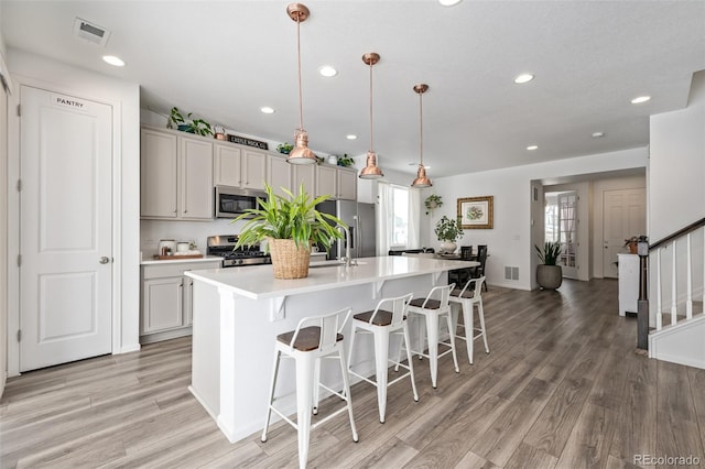 kitchen featuring appliances with stainless steel finishes, a breakfast bar, pendant lighting, an island with sink, and light hardwood / wood-style floors