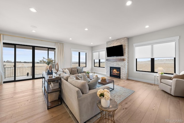 living area featuring light wood finished floors, a stone fireplace, baseboards, and recessed lighting