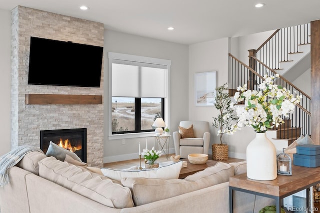 living area with stairway, recessed lighting, a stone fireplace, and wood finished floors