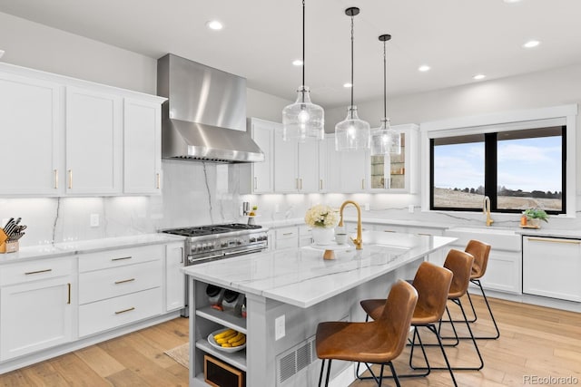 kitchen featuring range with two ovens, white dishwasher, white cabinetry, light wood-style floors, and wall chimney exhaust hood