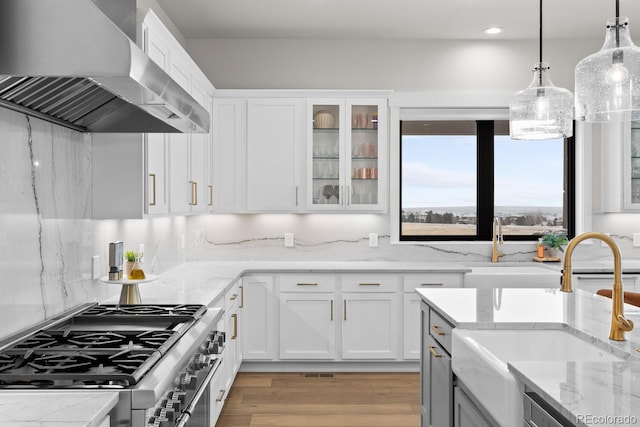 kitchen featuring a sink, white cabinets, high end stainless steel range, wall chimney exhaust hood, and pendant lighting