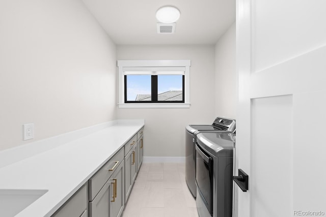 clothes washing area featuring visible vents, washing machine and clothes dryer, cabinet space, and baseboards