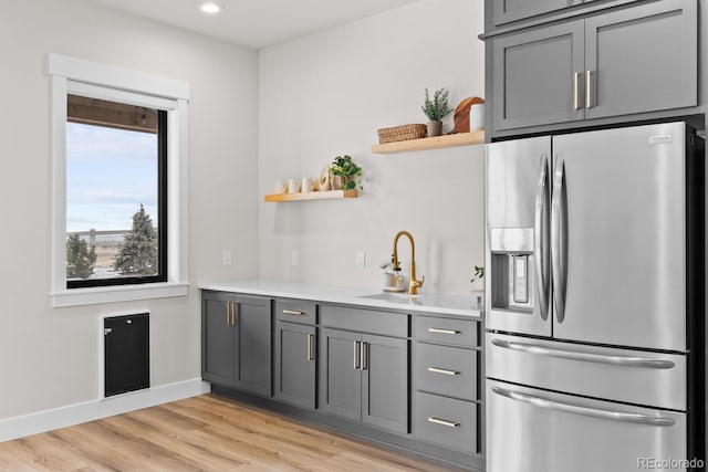 kitchen with open shelves, gray cabinets, light wood-style floors, a sink, and stainless steel fridge with ice dispenser