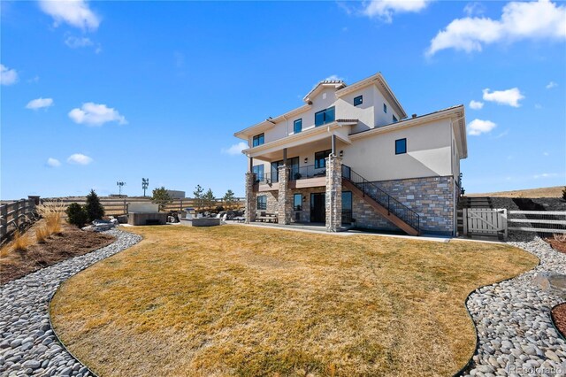 rear view of property featuring a patio, fence, stairs, stone siding, and stucco siding