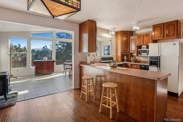 kitchen featuring sink, white refrigerator with ice dispenser, kitchen peninsula, light hardwood / wood-style floors, and a breakfast bar area