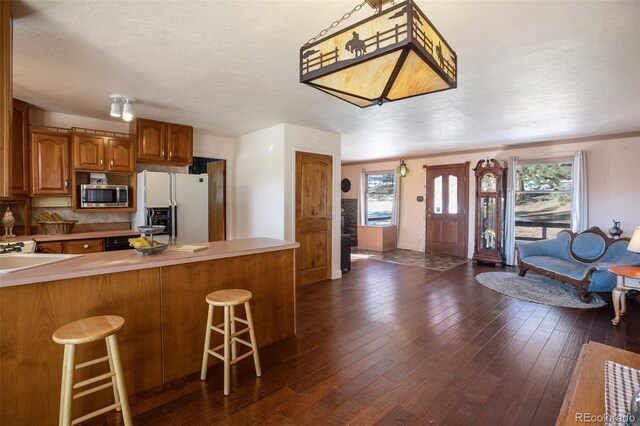 kitchen featuring kitchen peninsula, dark hardwood / wood-style flooring, a textured ceiling, white fridge with ice dispenser, and a breakfast bar area