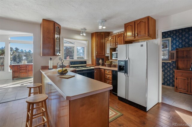 kitchen with hardwood / wood-style floors, plenty of natural light, a kitchen breakfast bar, and white appliances