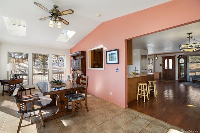 dining space with ceiling fan, vaulted ceiling with skylight, and light hardwood / wood-style floors