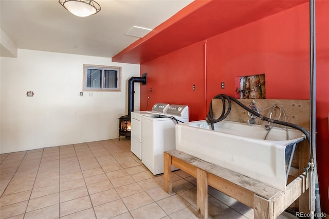 washroom with washing machine and clothes dryer, light tile patterned floors, a wood stove, and sink