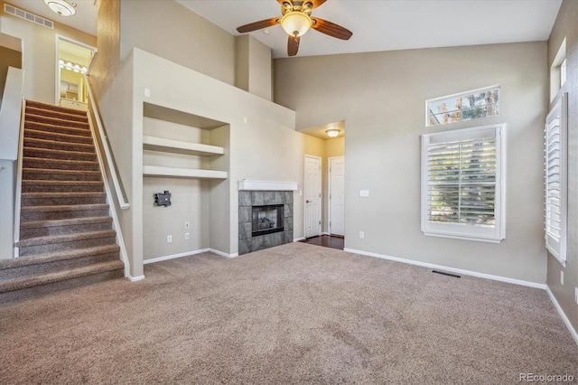 unfurnished living room with ceiling fan, high vaulted ceiling, carpet, and a tile fireplace