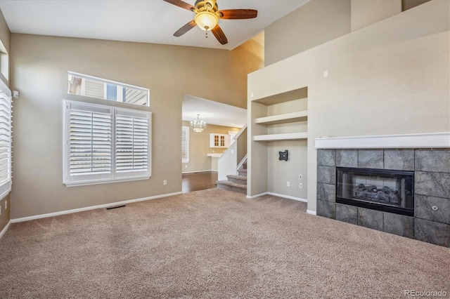 unfurnished living room featuring ceiling fan with notable chandelier, high vaulted ceiling, carpet floors, and a tile fireplace