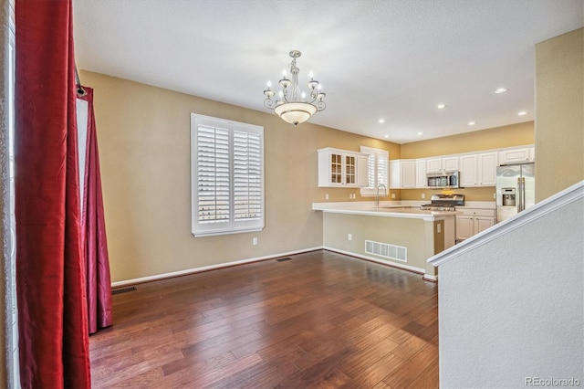 kitchen featuring dark hardwood / wood-style floors, white cabinets, kitchen peninsula, appliances with stainless steel finishes, and decorative light fixtures