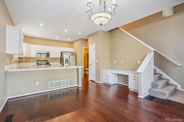 kitchen with kitchen peninsula, built in desk, white cabinetry, stainless steel appliances, and dark hardwood / wood-style floors