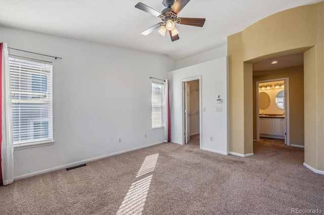 unfurnished bedroom with light carpet, ensuite bath, ceiling fan, and a walk in closet